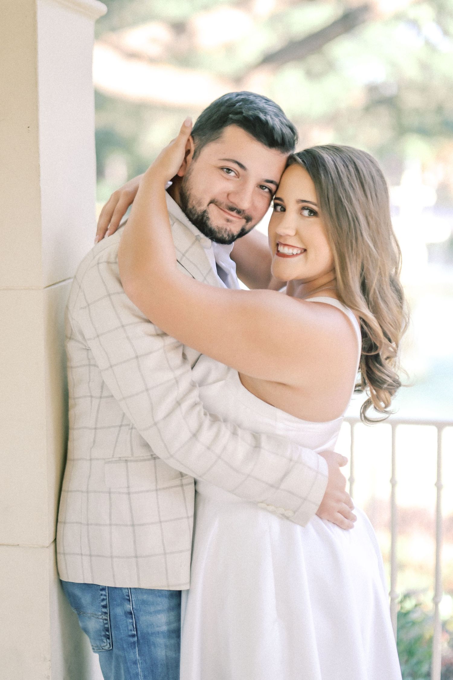 Smiling couple embracing closely beside a stone column during an outdoor engagement photo session.