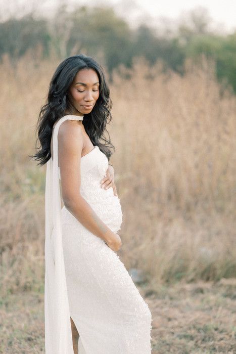 A dreamy outdoor maternity session captures a flowing white dress against dried winter grass.