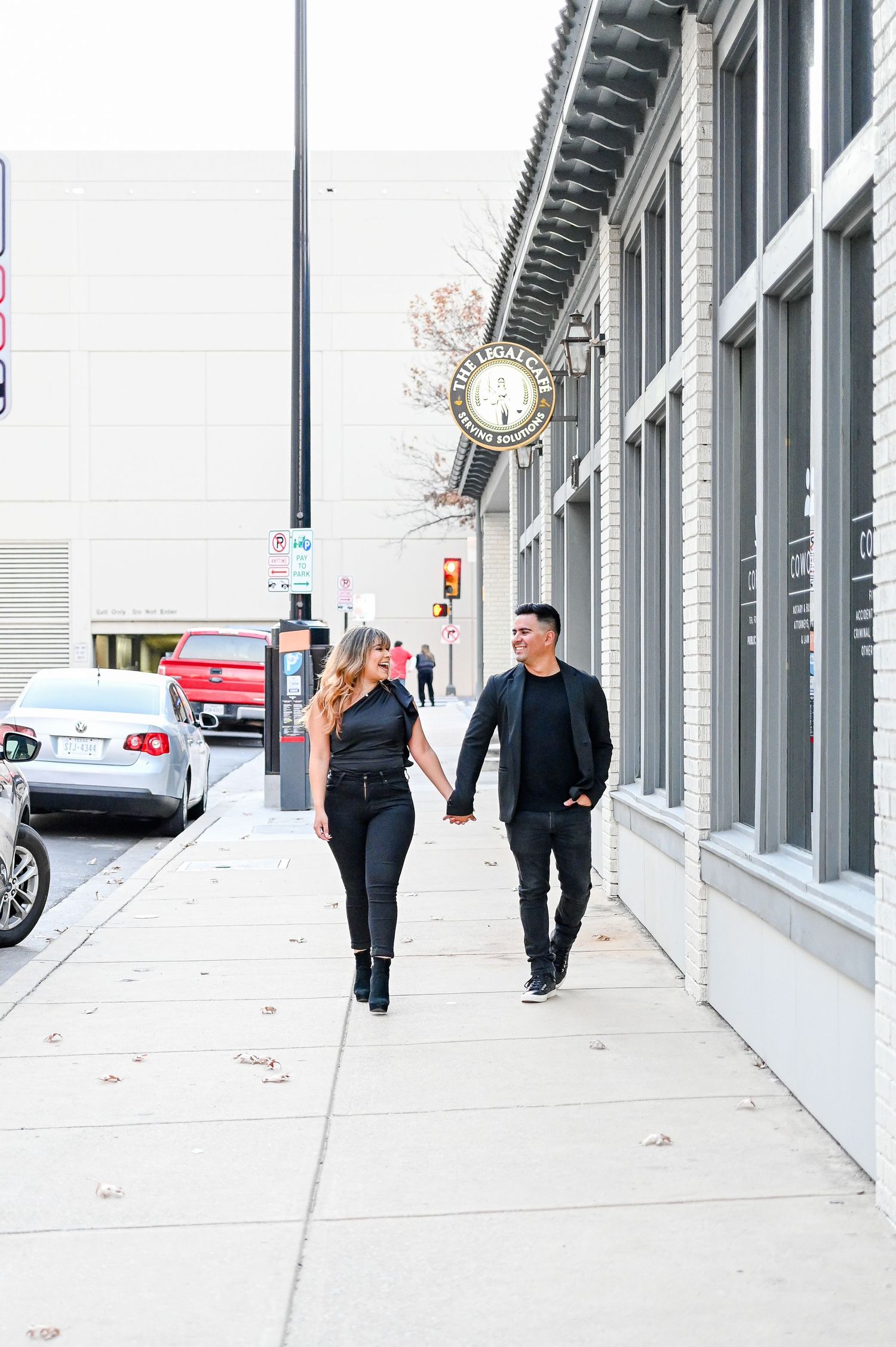 Happy couple holding hands and walking along a city sidewalk past a historic clock building.