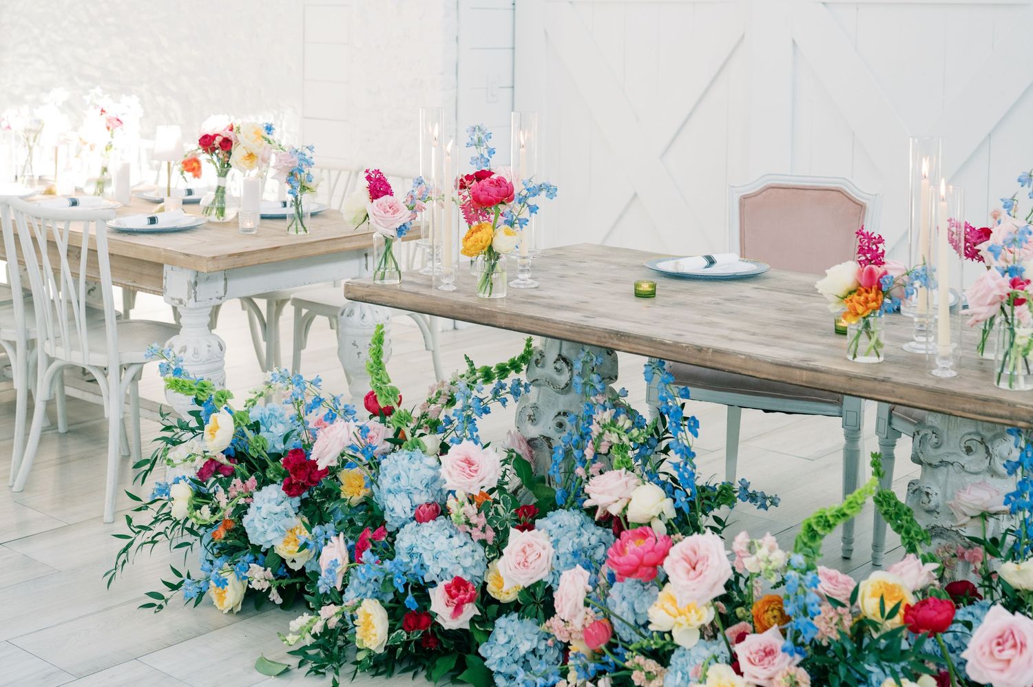 Elegant wedding reception tables adorned with lush blue, pink, and colorful floral arrangements and white candles.