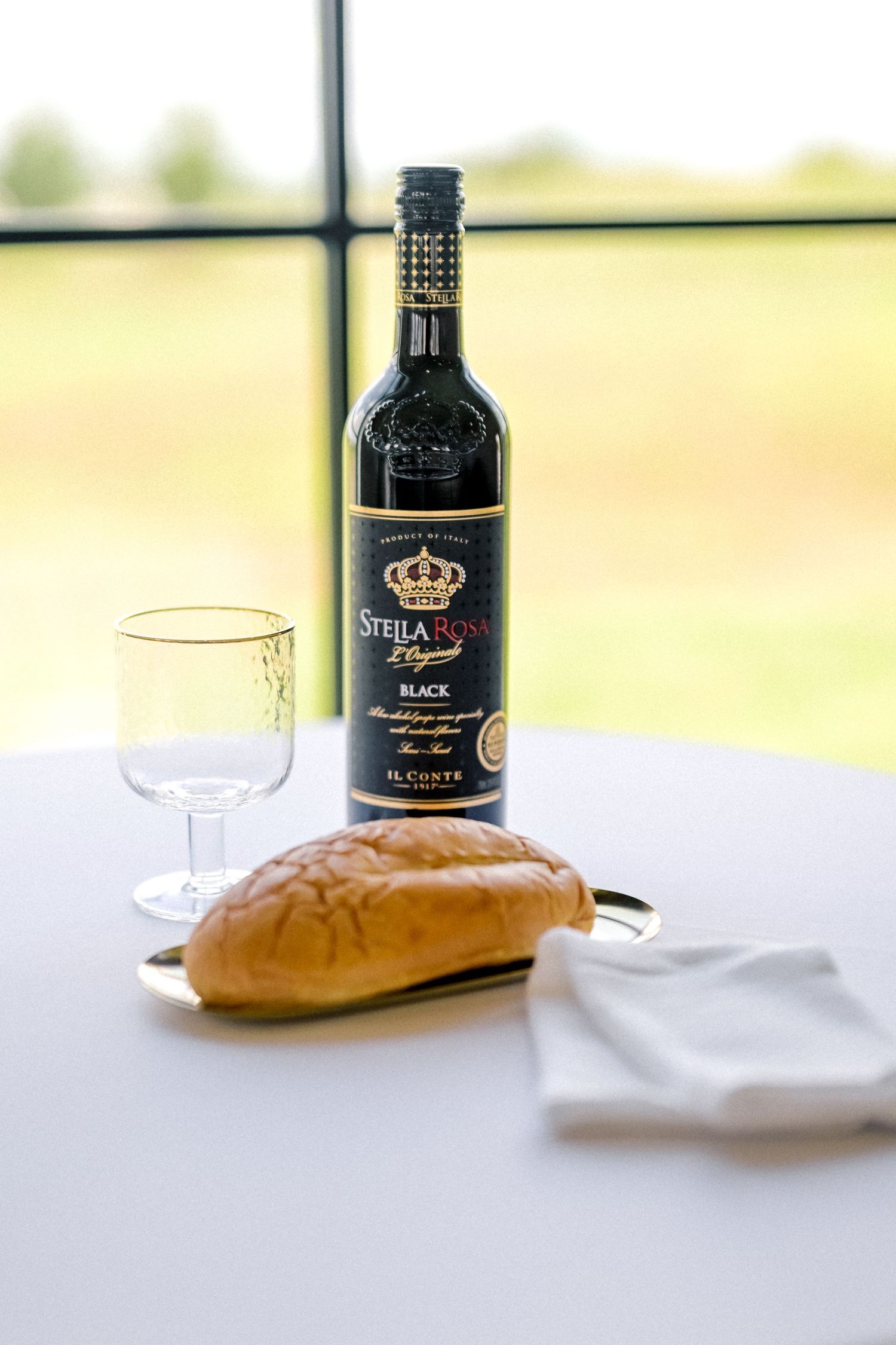 Stella Rosa Black wine bottle with bread and glass on a white tablecloth.