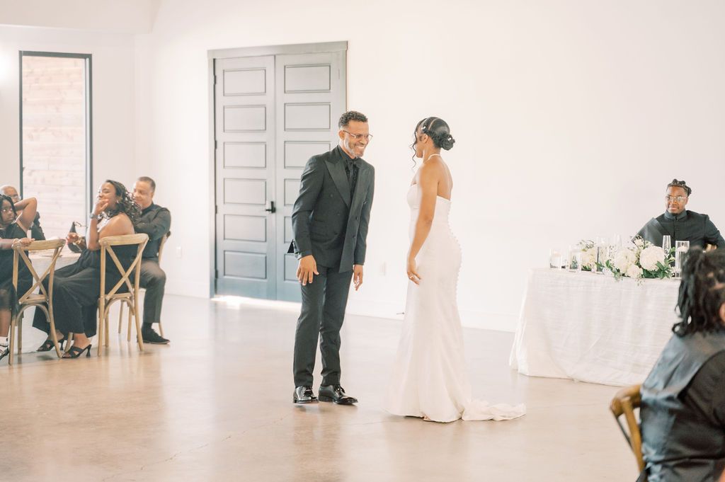 Bride and groom share a joyful moment during their wedding reception in an elegant white venue.