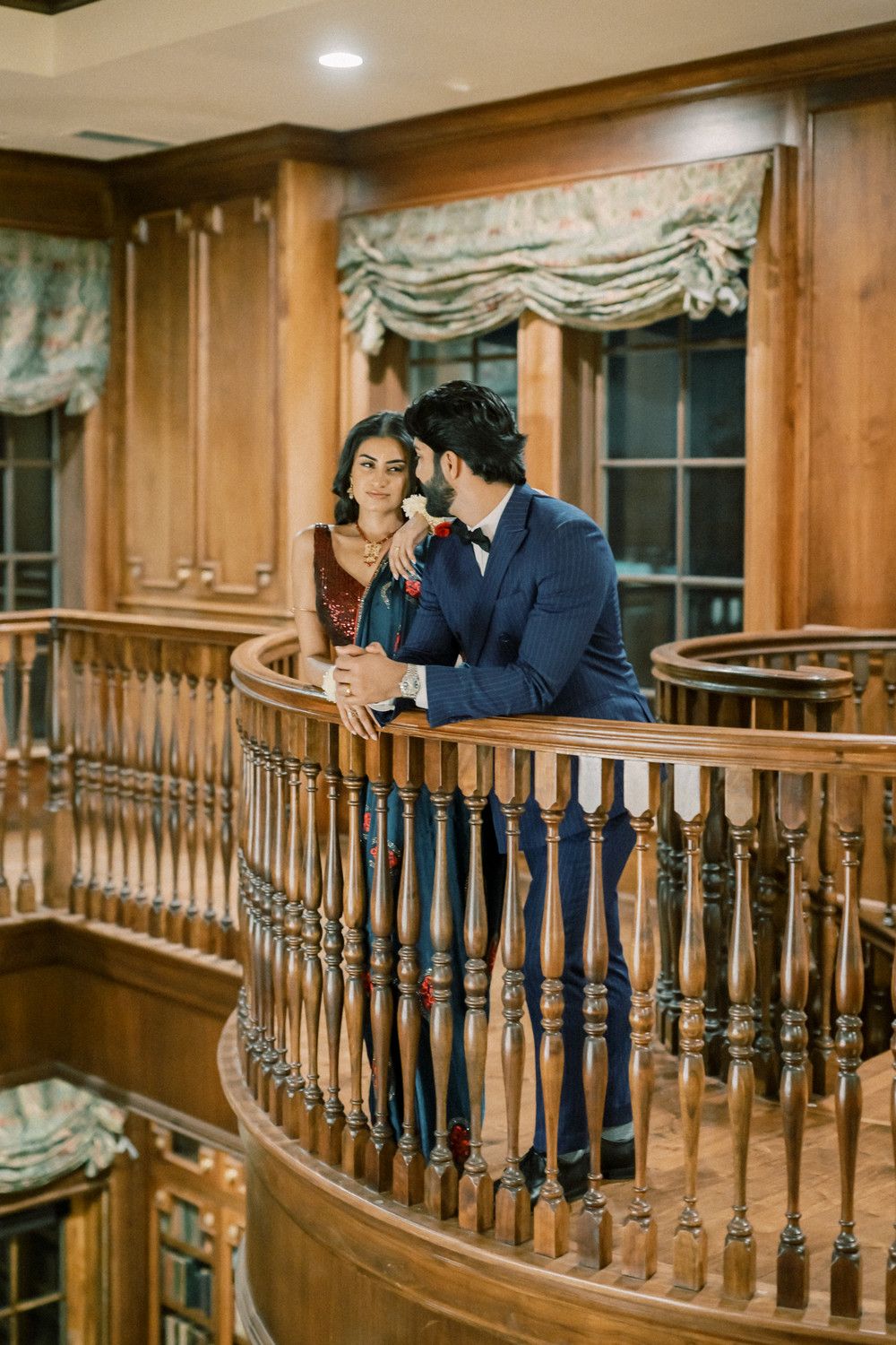Couple shares intimate moment on curved wooden balcony in formal indoor setting.