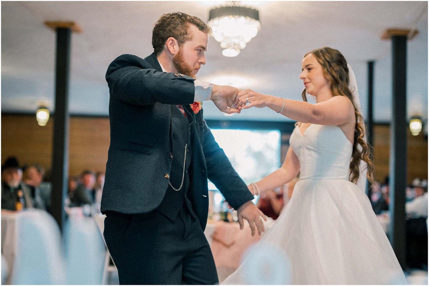 Couple dancing together in a ballroom under a crystal chandelier during their wedding celebration.
