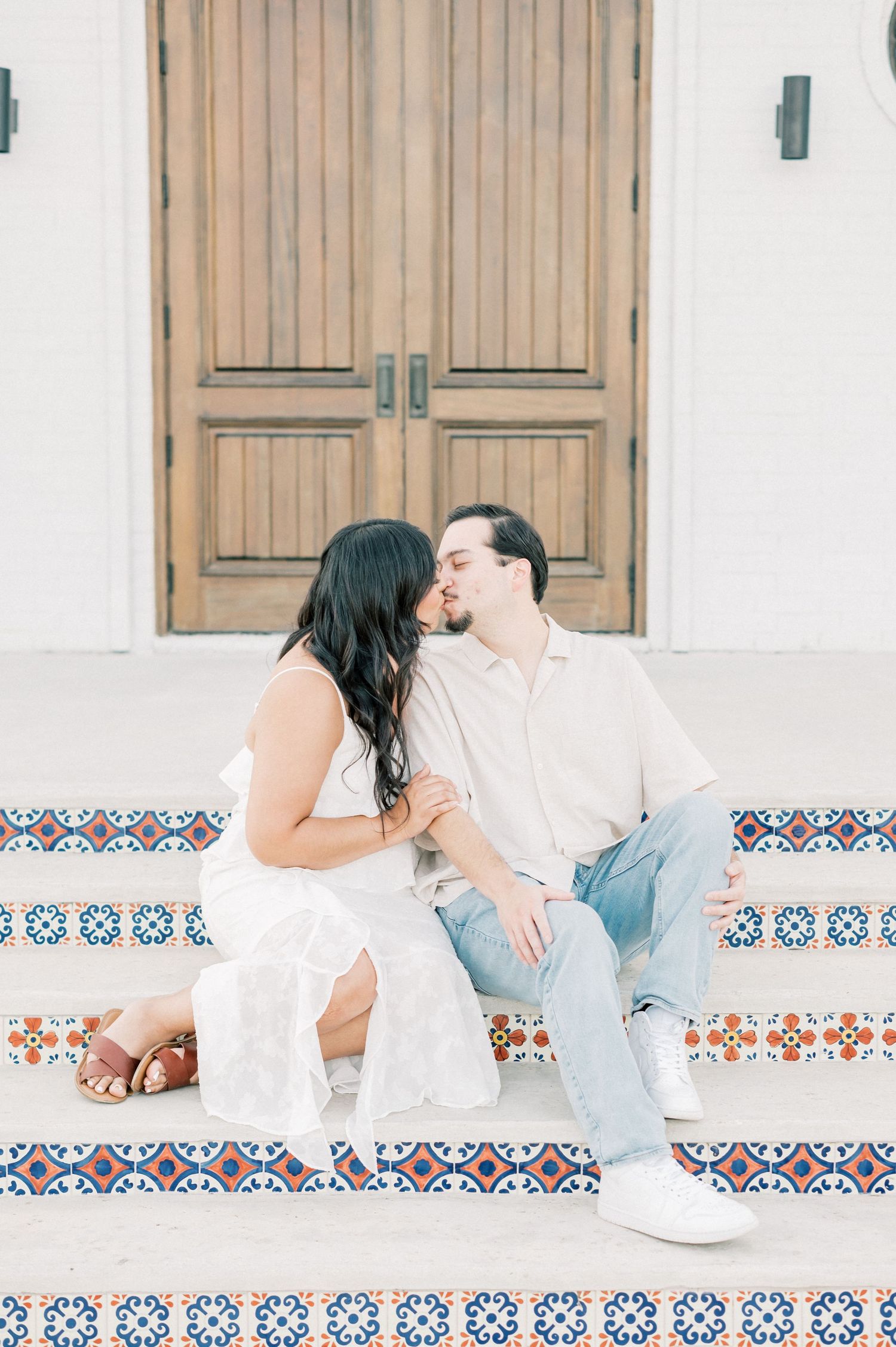 Couple in white and blue outfits sitting on decorative tiled steps sharing a romantic moment together.