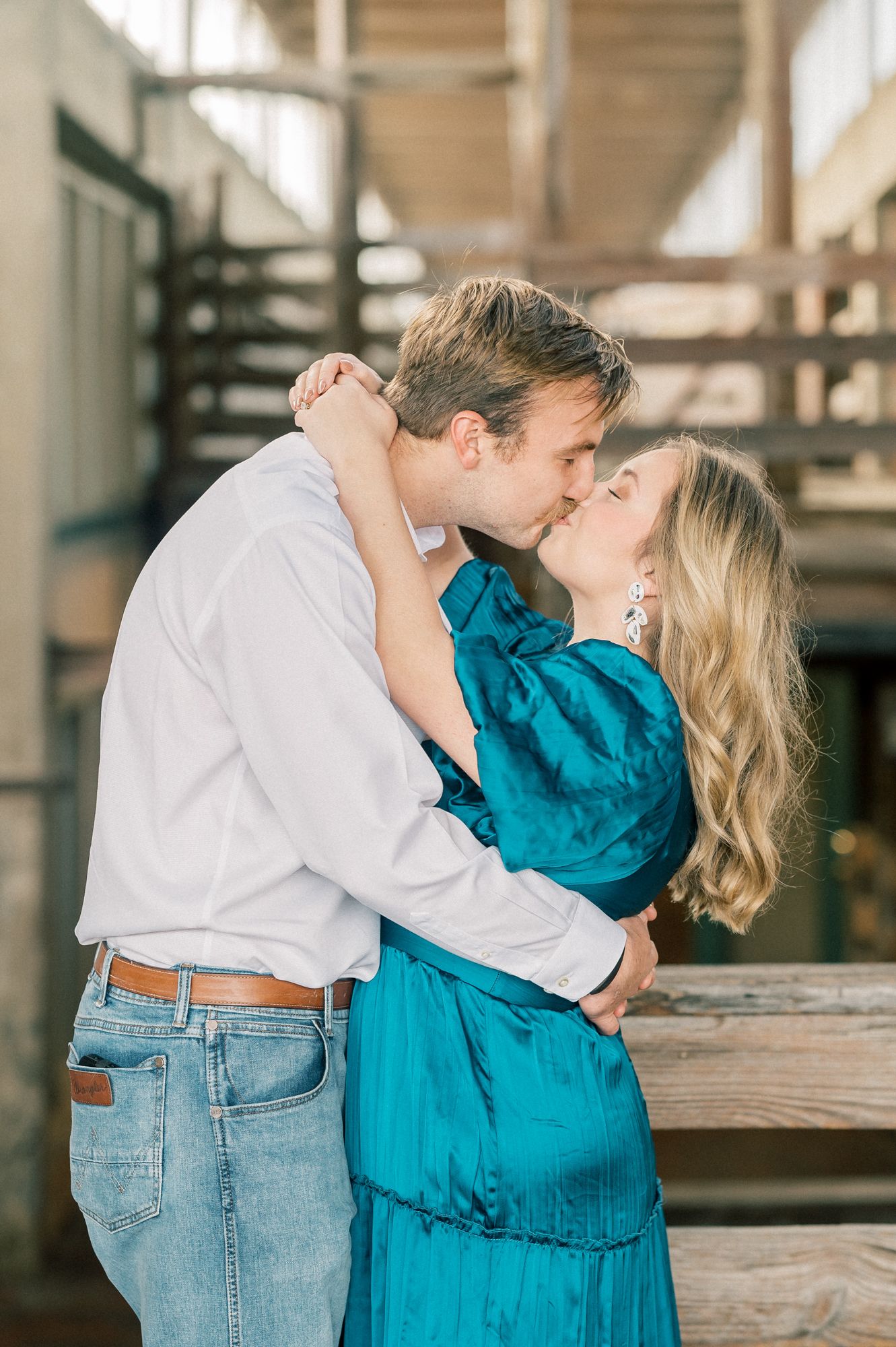 A romantic kiss captured between a couple in a rustic industrial setting with natural lighting.