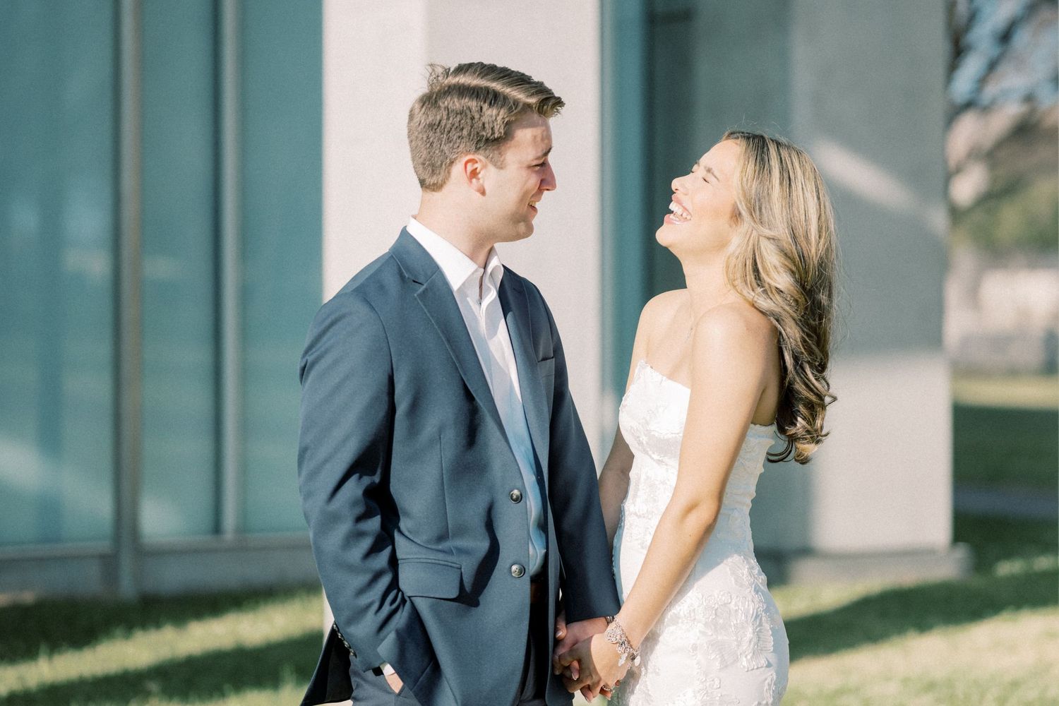 A joyful couple shares a candid moment together on their wedding day, dressed in formal attire outdoors.