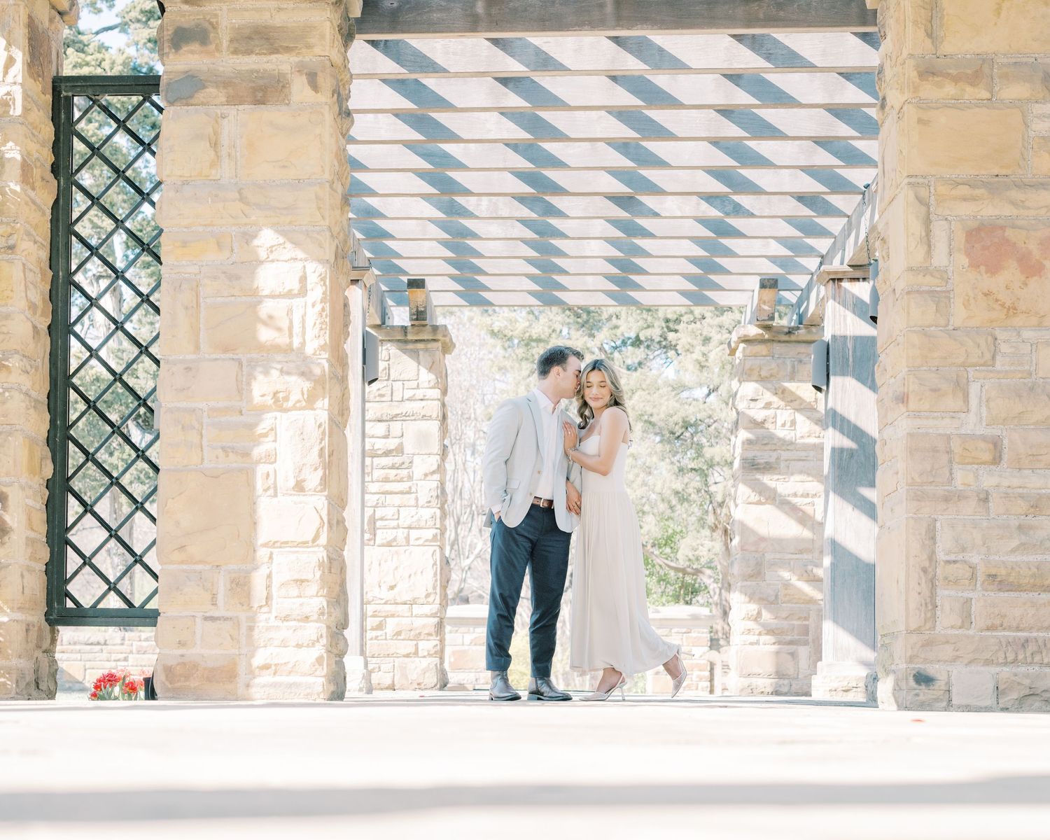 A couple shares a romantic moment under a stone archway during their outdoor wedding ceremony.