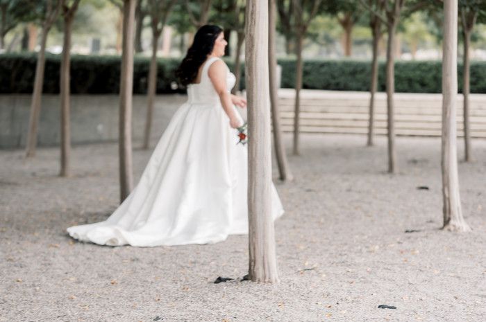Bride in elegant white ball gown with train poses beside a tree in a serene outdoor park setting.