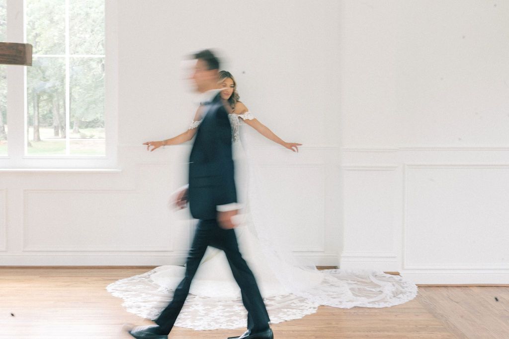 Blurred motion photo of bride and groom walking together in bright white wedding venue.