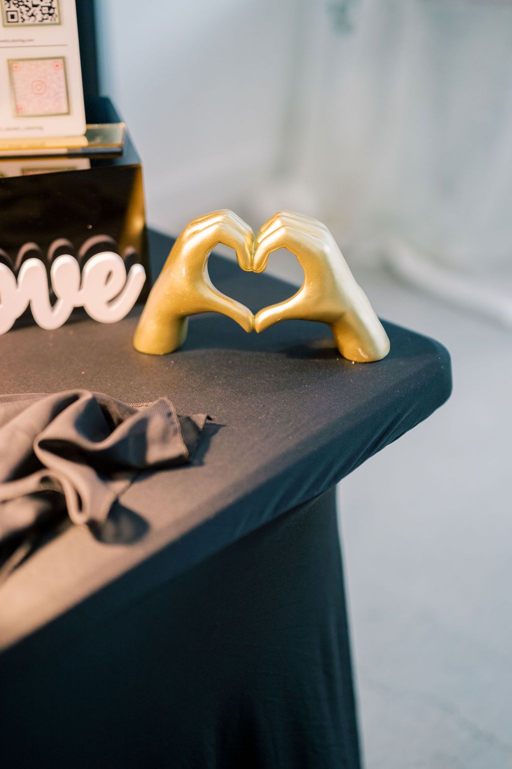 Gold ceramic hands forming a heart shape on a dark tablecloth, with a decorative love sign in the background.