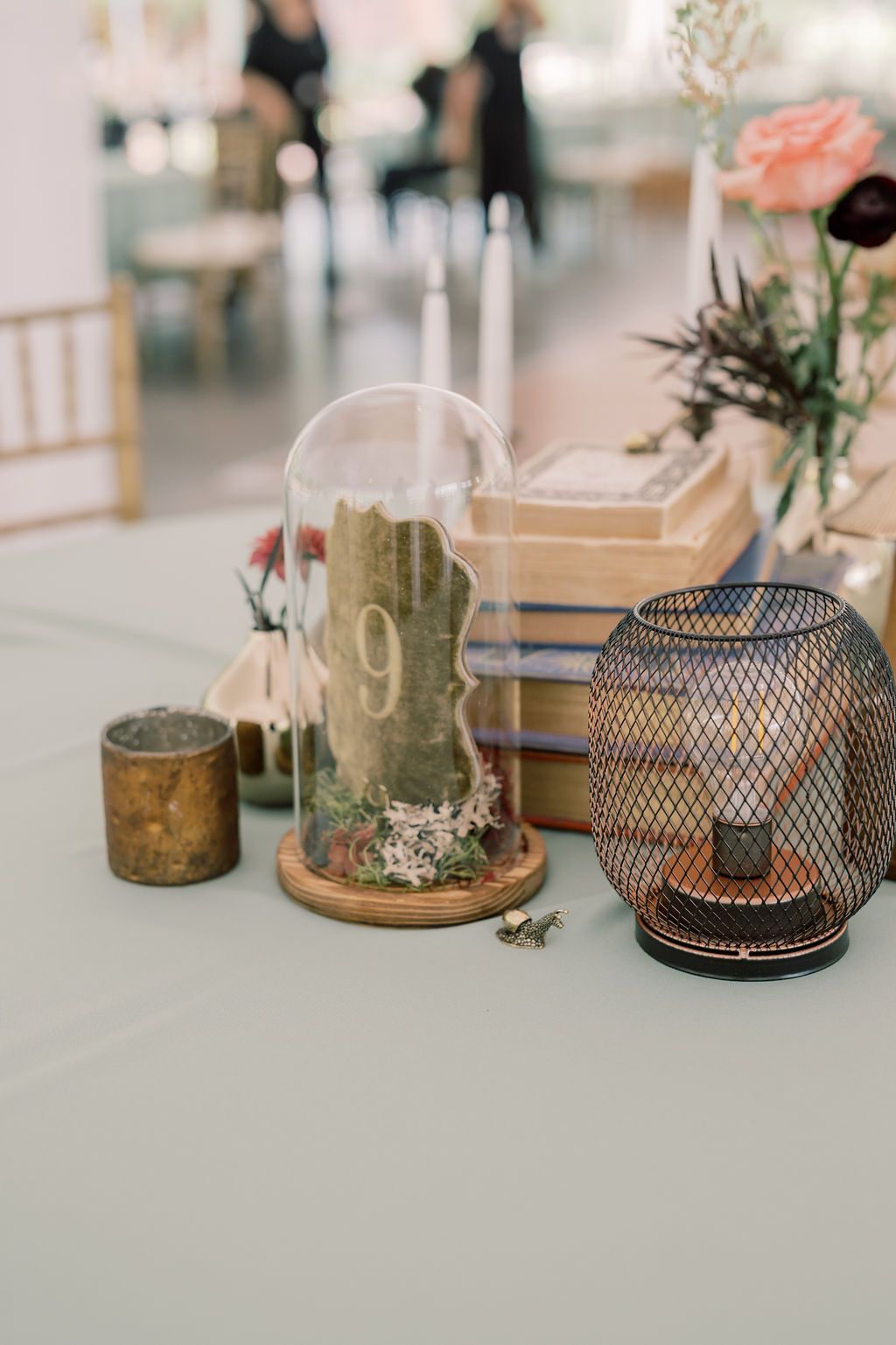 Rustic wedding table centerpiece with glass cloche table number 9, mesh lantern, gold candles, and stacked books.