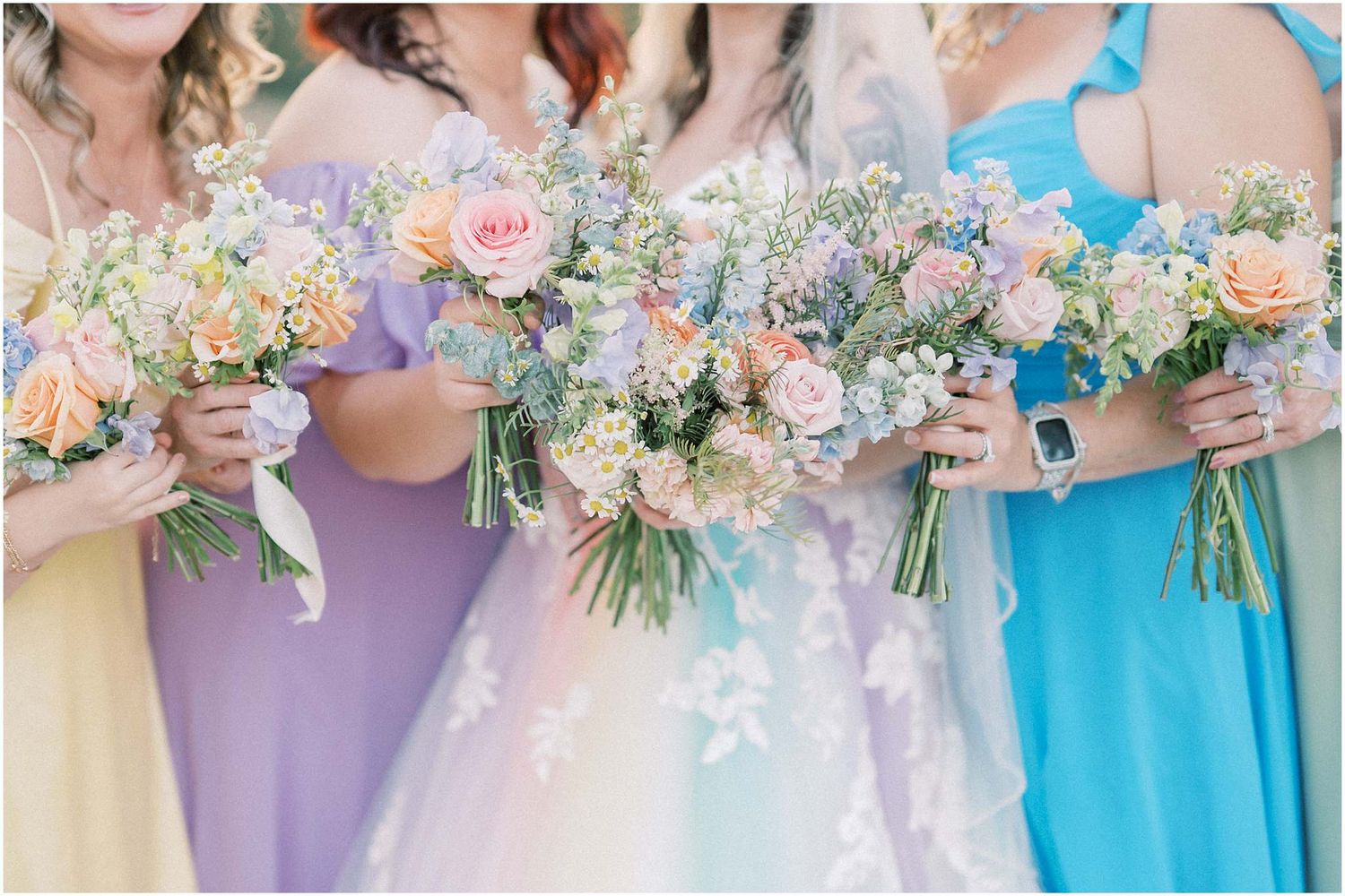 Bridesmaids holding pastel bouquets in coordinating blue and purple dresses.