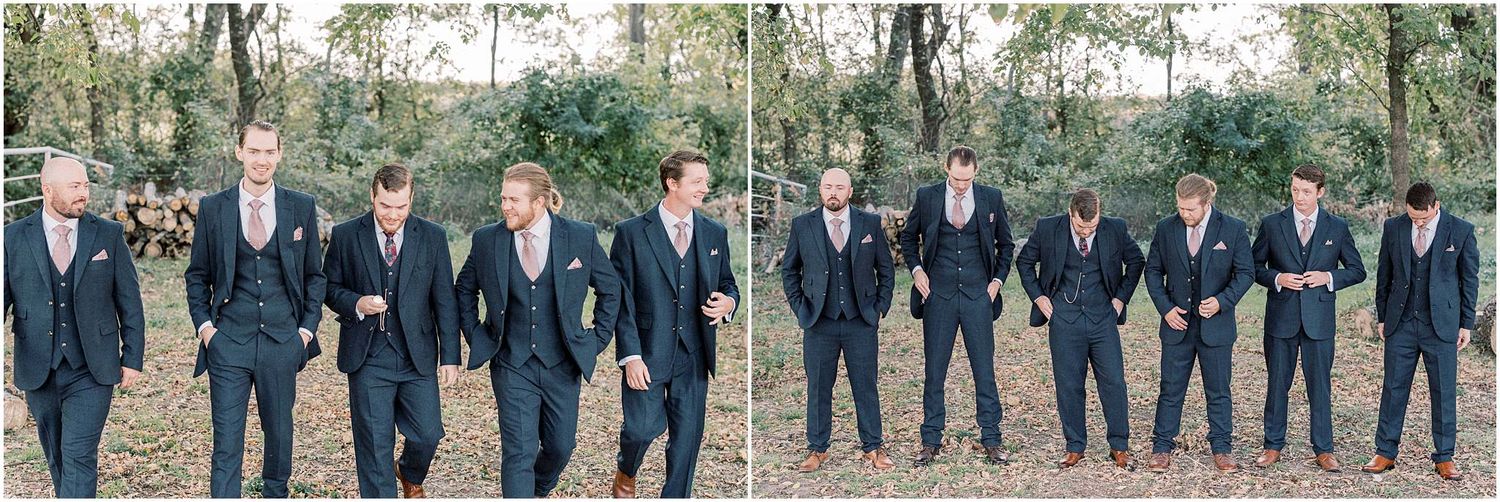 Large wedding party in navy suits and formal attire poses together outdoors.