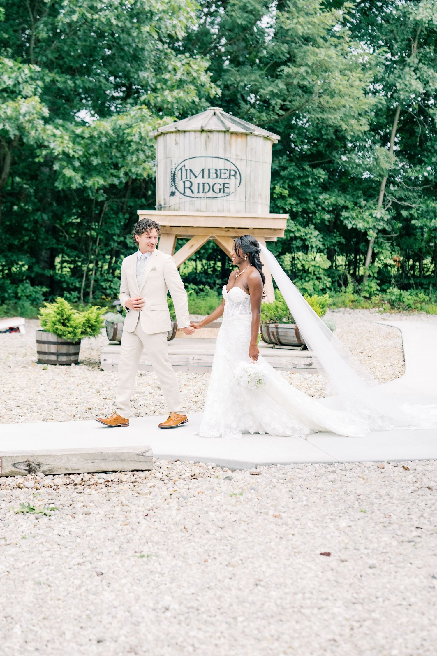 Bride and groom holding hands at Timber Ridge venue, bride in lace gown with veil, groom in cream suit.