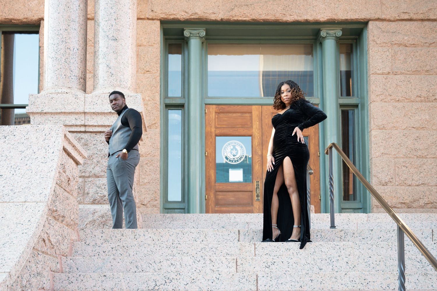 Elegant couple posing on stone steps outside a government building, man in gray suit, woman in black dress.