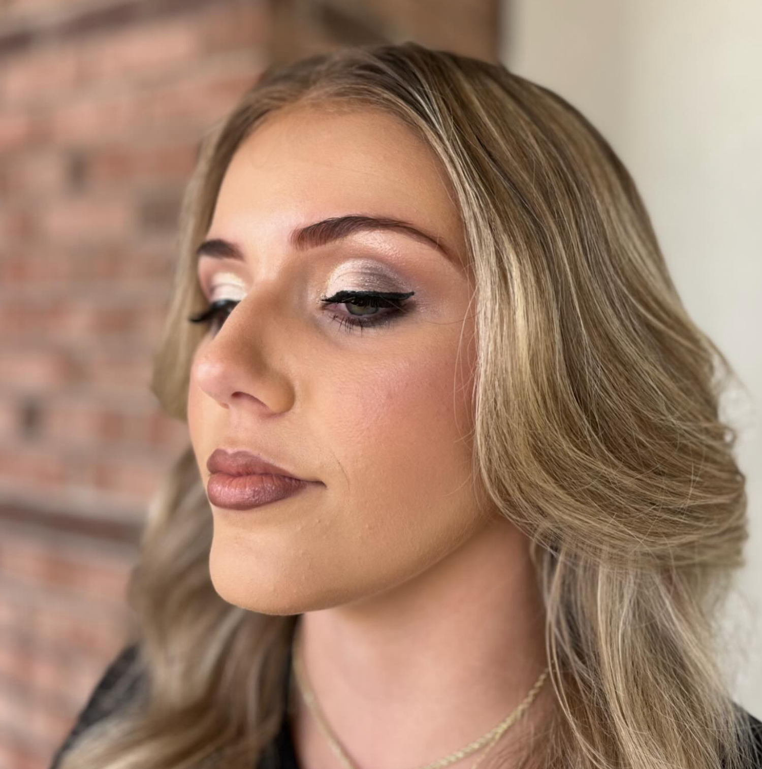 Woman with blonde hair showcasing elegant makeup featuring winged eyeliner, subtle eyeshadow, and nude lips.