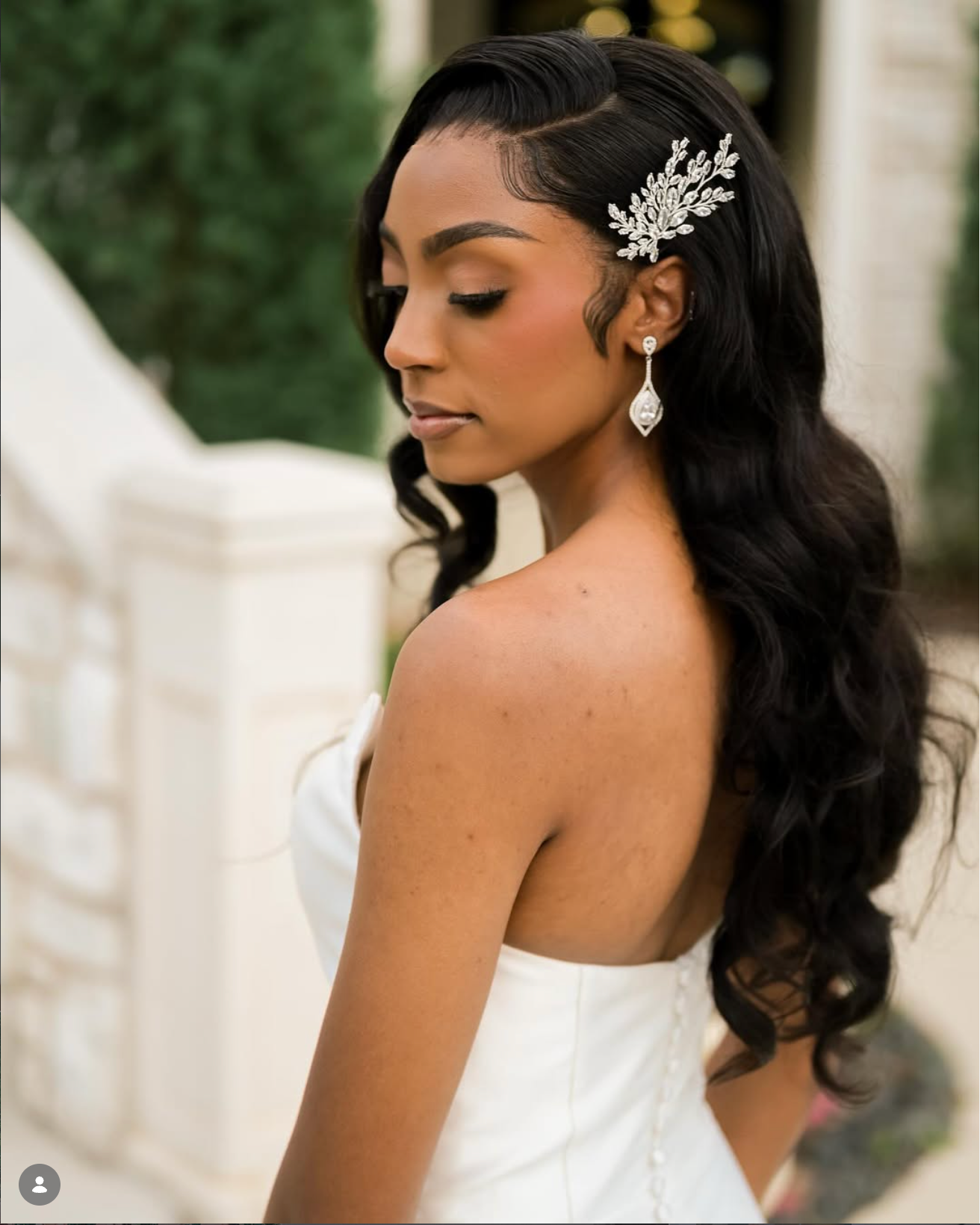 Bride with long wavy black hair adorned with a crystal hair comb and teardrop earrings in a white strapless gown.