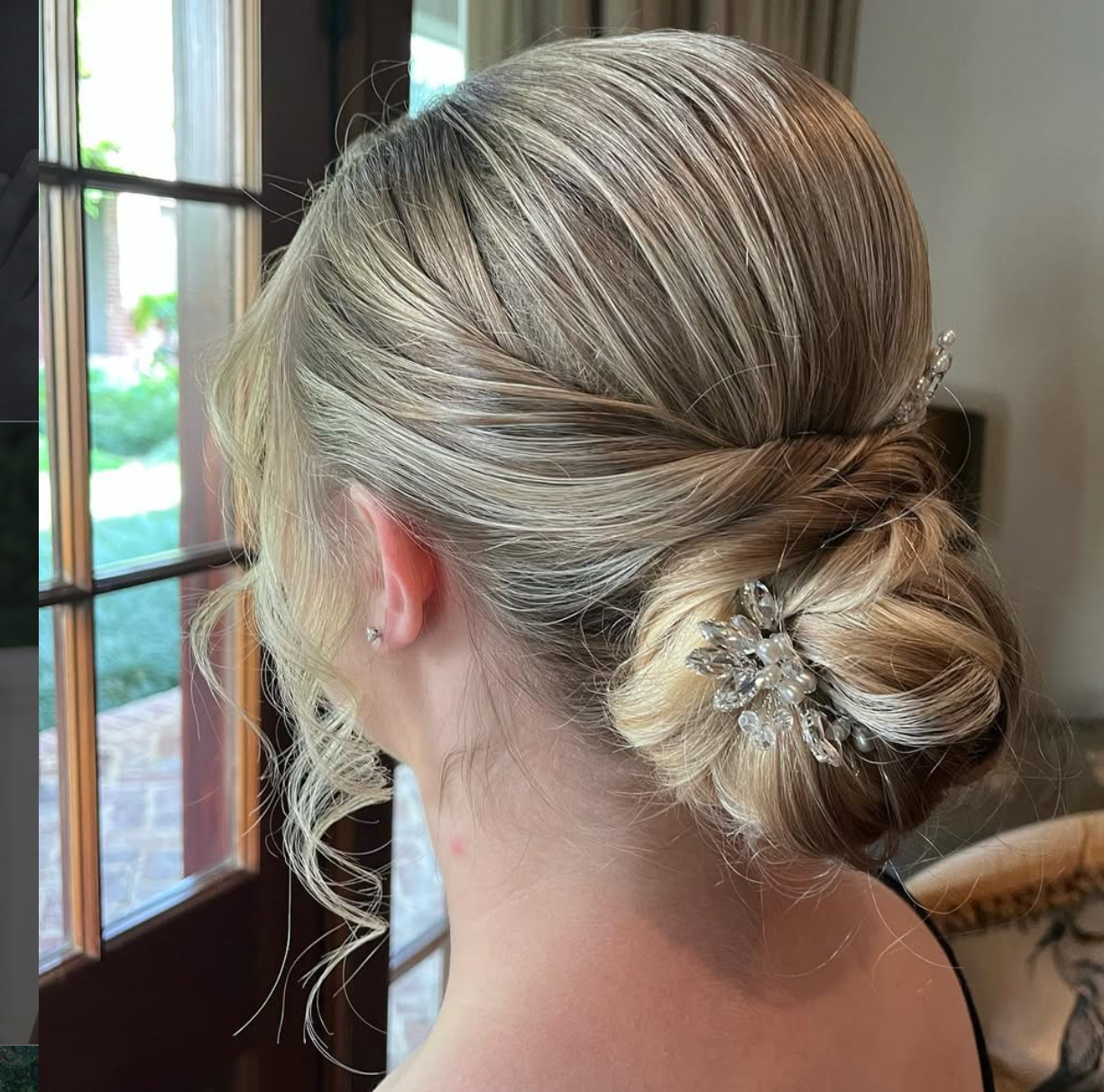 Elegant bridal updo with a crystal hair pin, featuring a low chignon and soft blonde highlights.