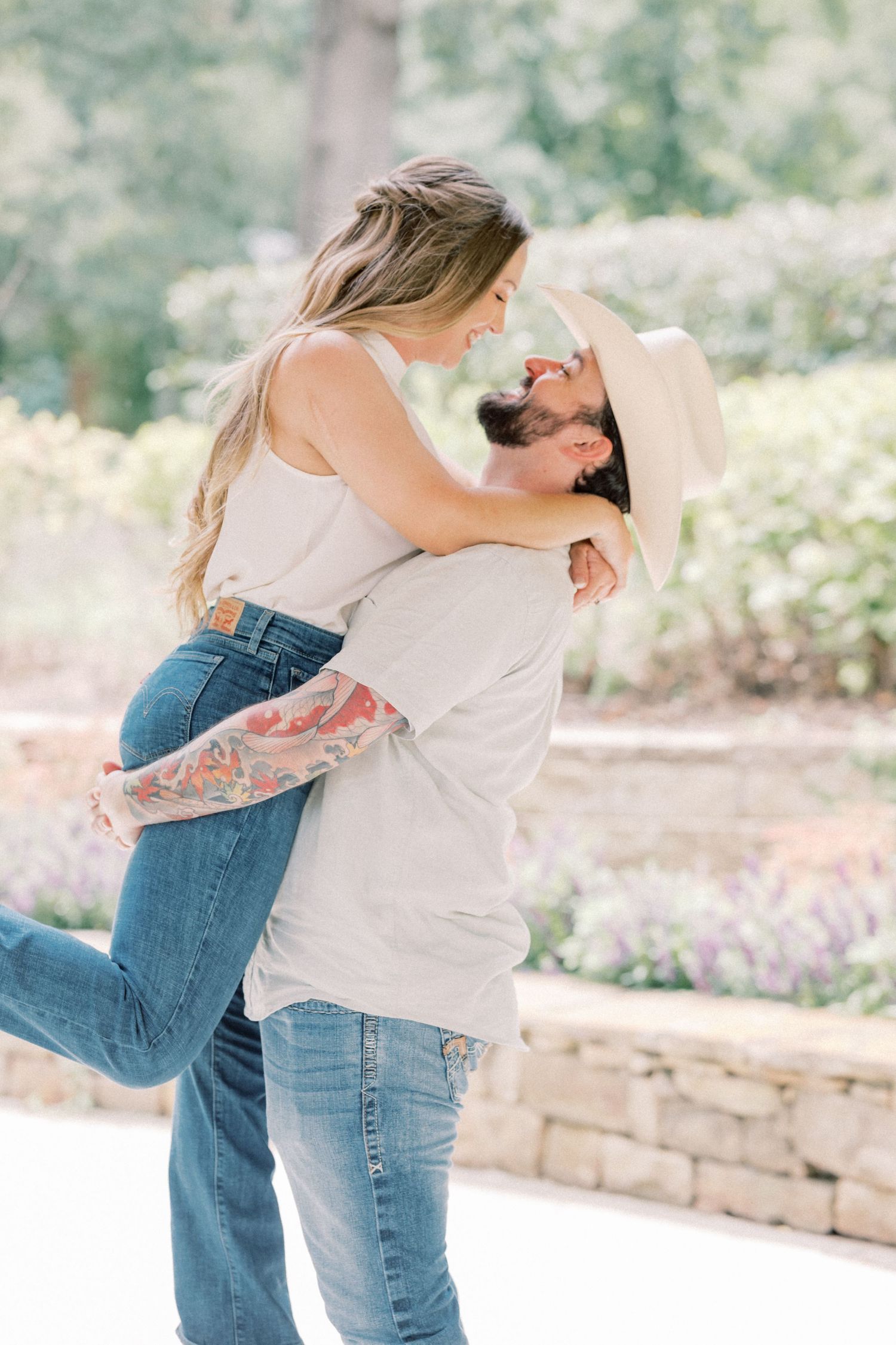Man lifting woman in a joyful embrace outdoors, both smiling with a garden backdrop.