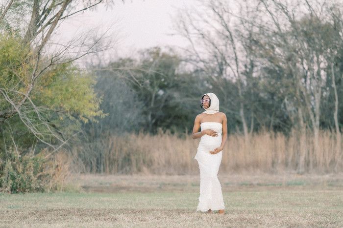 Distant view of maternity shoot in natural field setting with white dress.