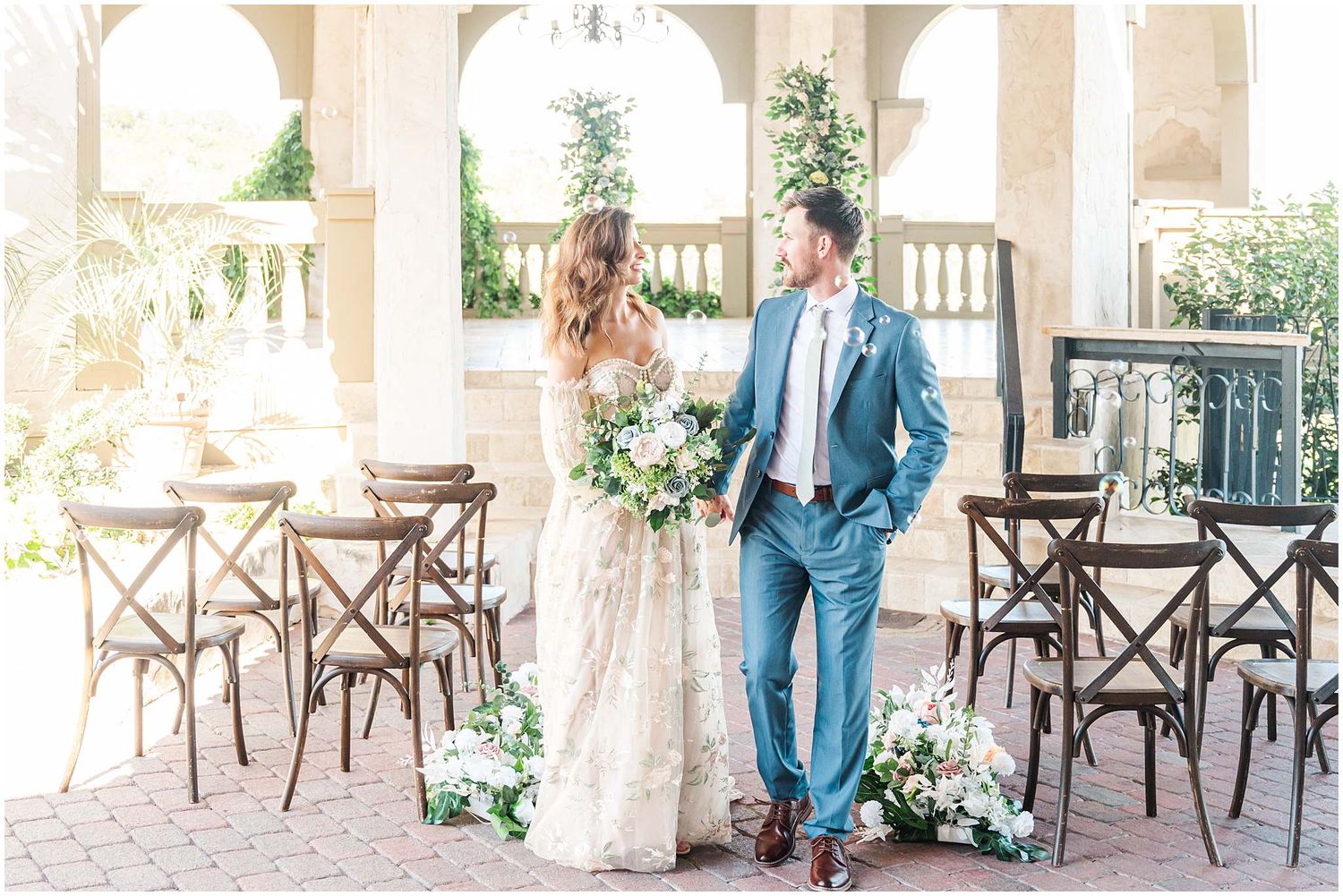 Sunlit courtyard wedding venue with white columns and rustic wooden seating arrangements.