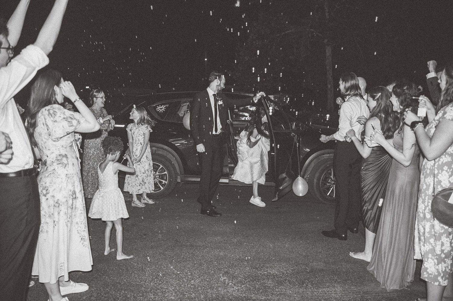 Black and white photo of wedding guests celebrating during a sparkler send-off exit.