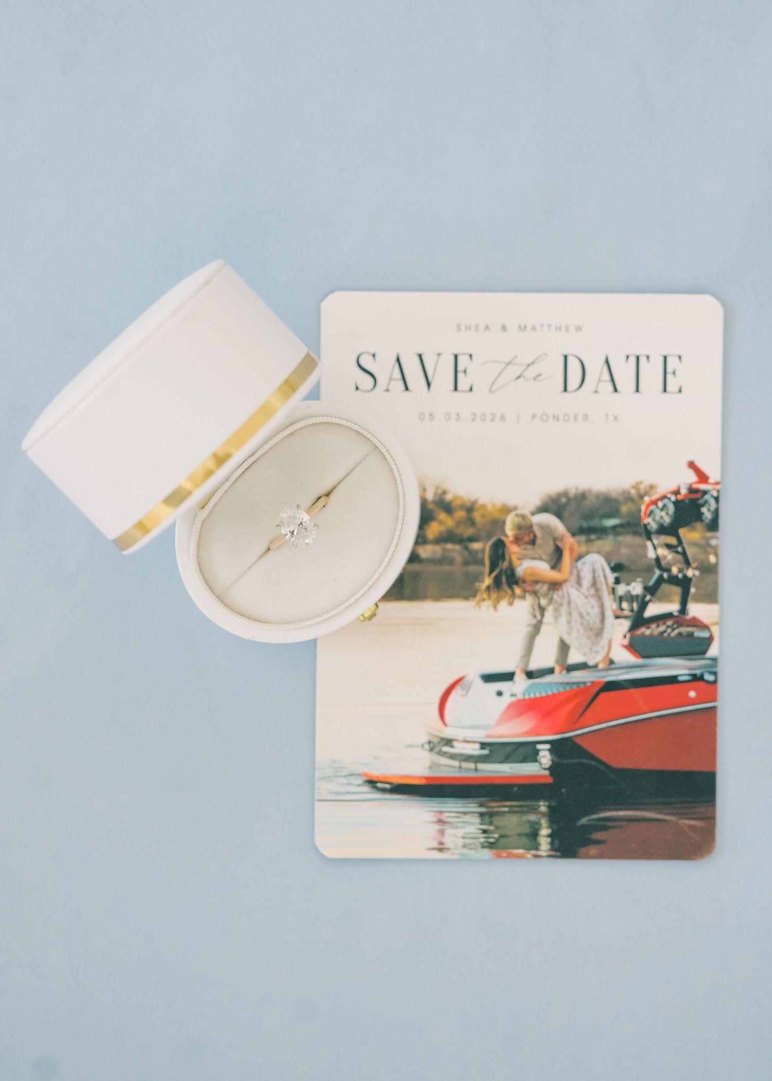 Save the date card featuring a couple kissing on a red boat, displayed with a diamond engagement ring in a white box.