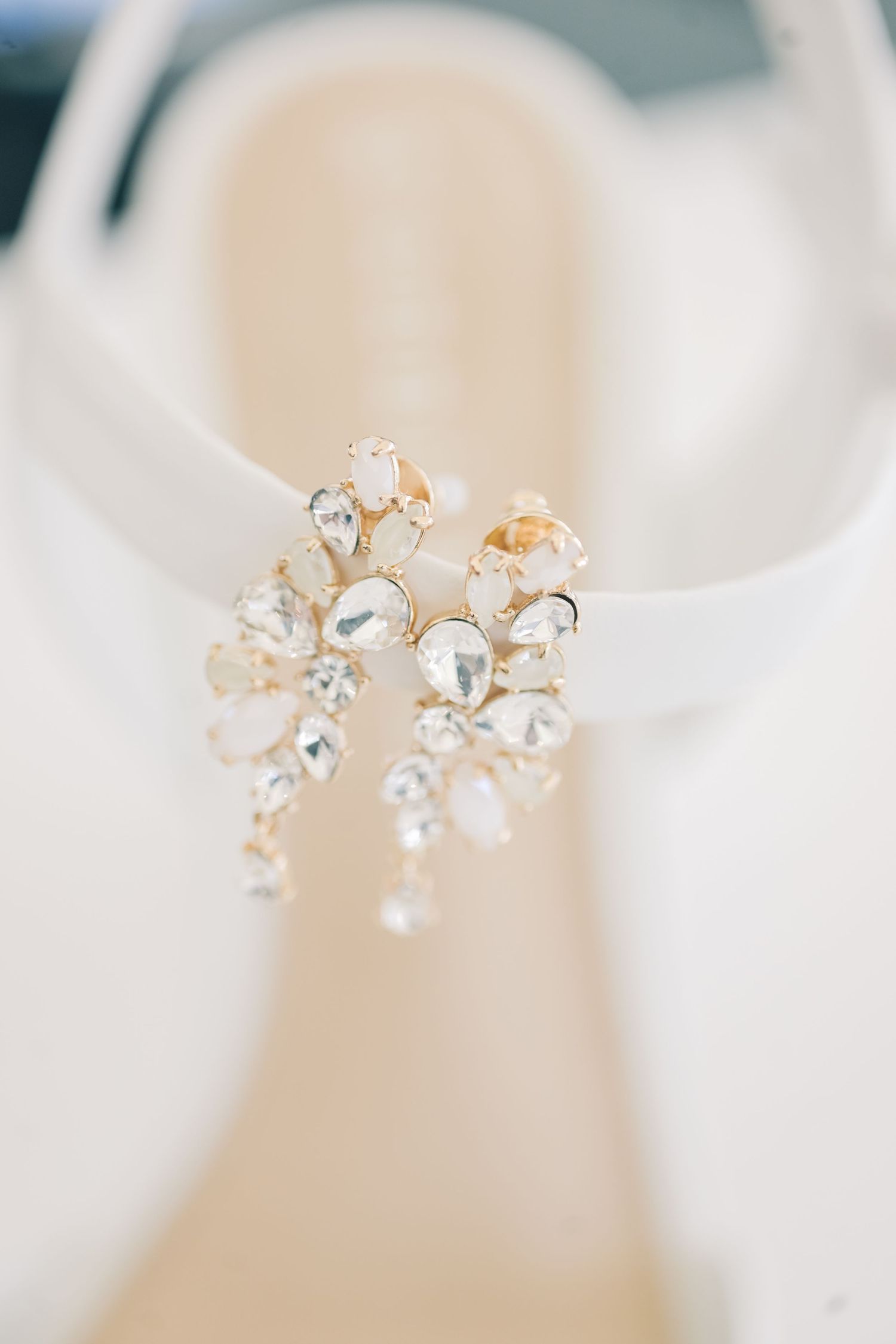 Crystal and gold bridal earrings with teardrop gemstones displayed on white wedding heels.