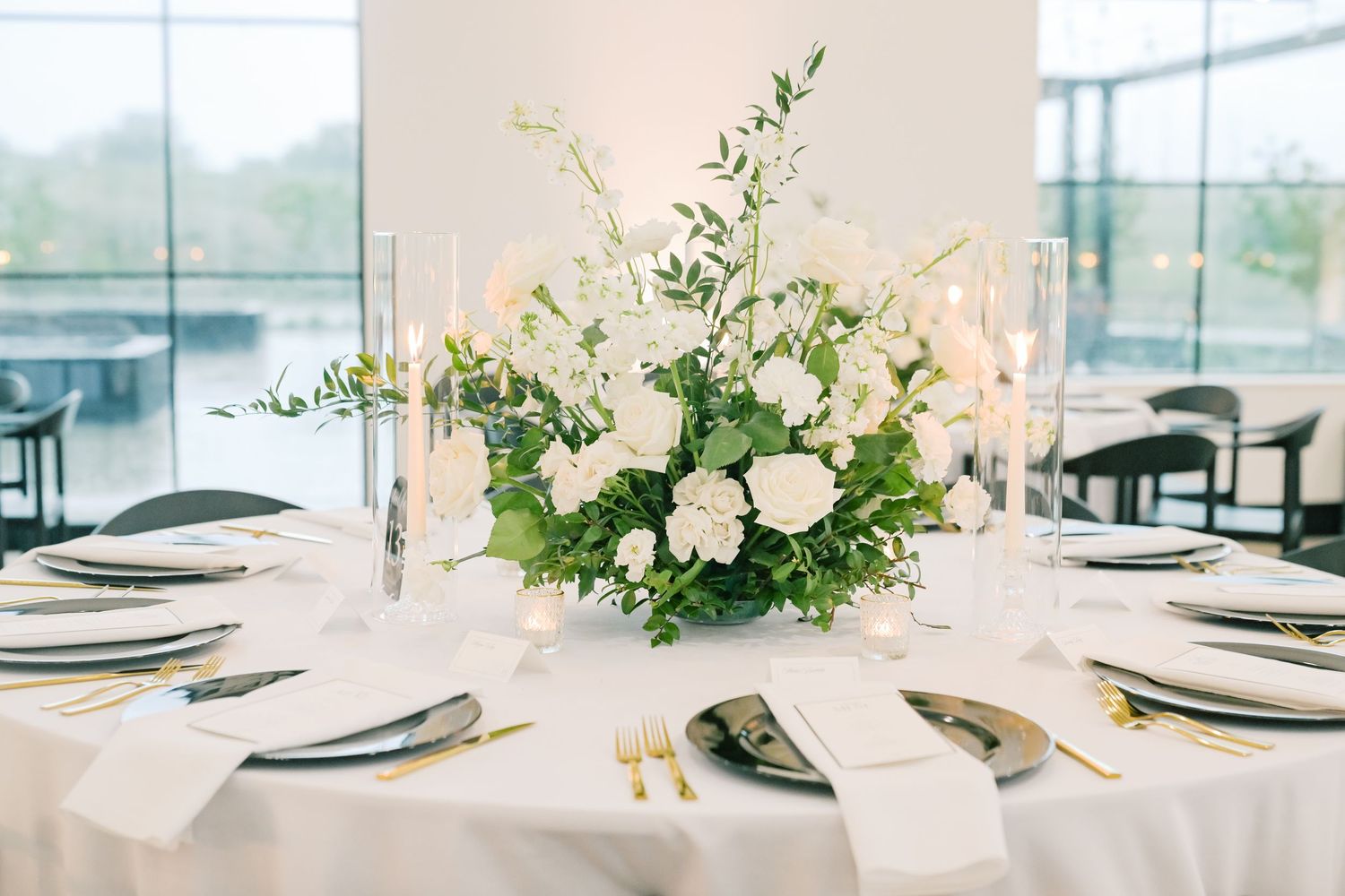 Elegant wedding reception table with white floral centerpiece, greenery, candles, and gold flatware.