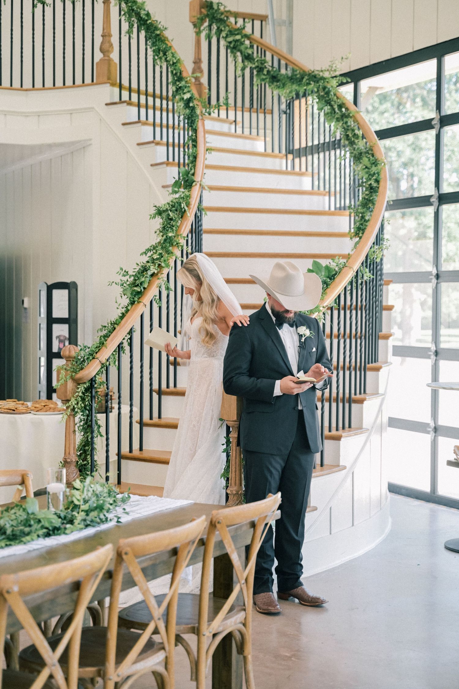 Bride and groom sharing private vows by a spiral staircase decorated with lush greenery garland.