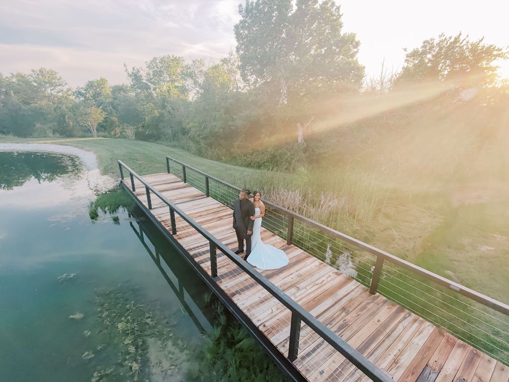 Couple sharing a romantic moment on a wooden dock over a serene lake surrounded by lush trees at golden hour.