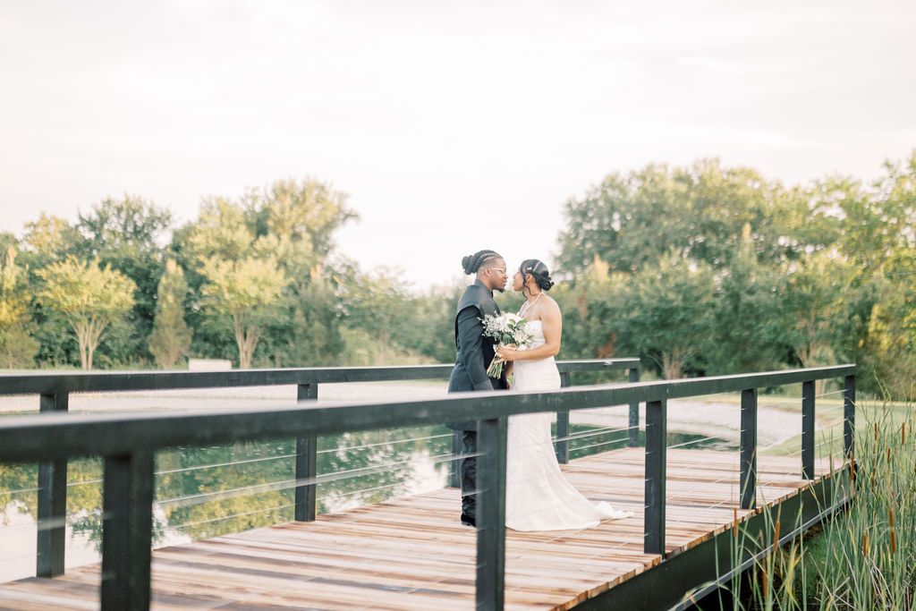 Bride and groom share a romantic moment on a wooden bridge surrounded by lush greenery and a serene pond.