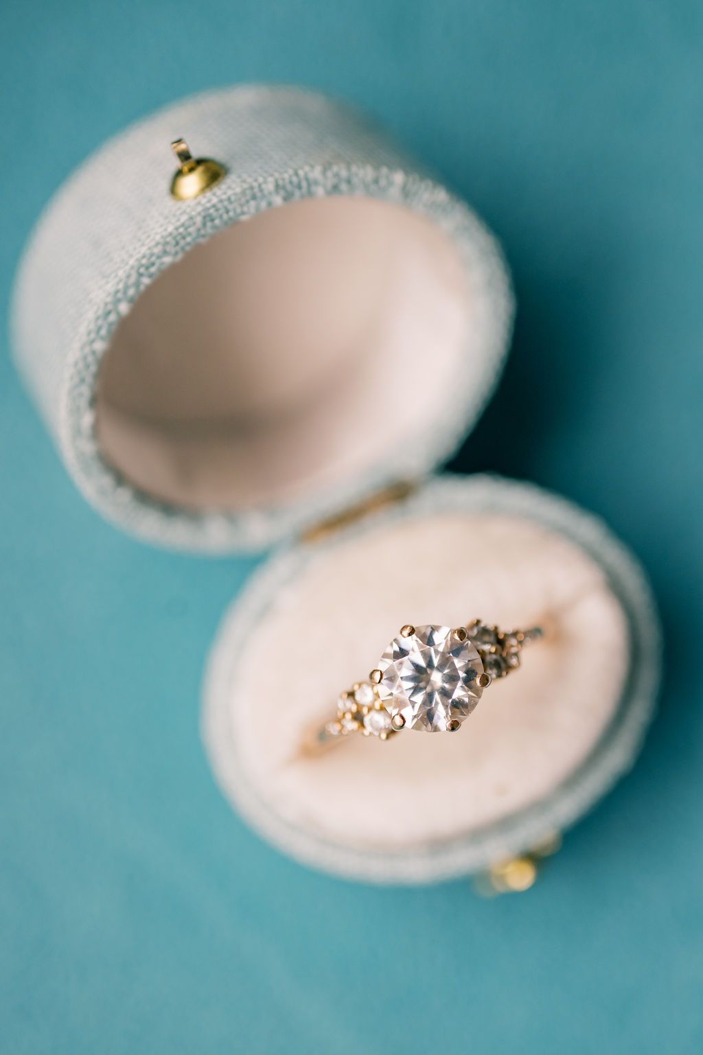 Round diamond engagement ring with floral gold band displayed in an open blue velvet ring box.