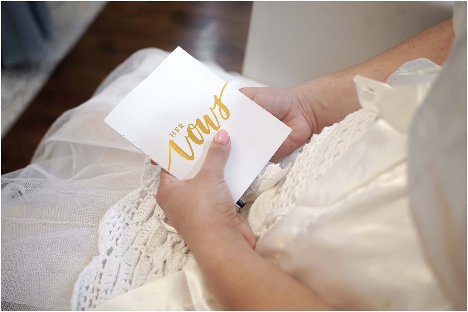 Bride in white dress reading gold calligraphy vows card on her wedding day.