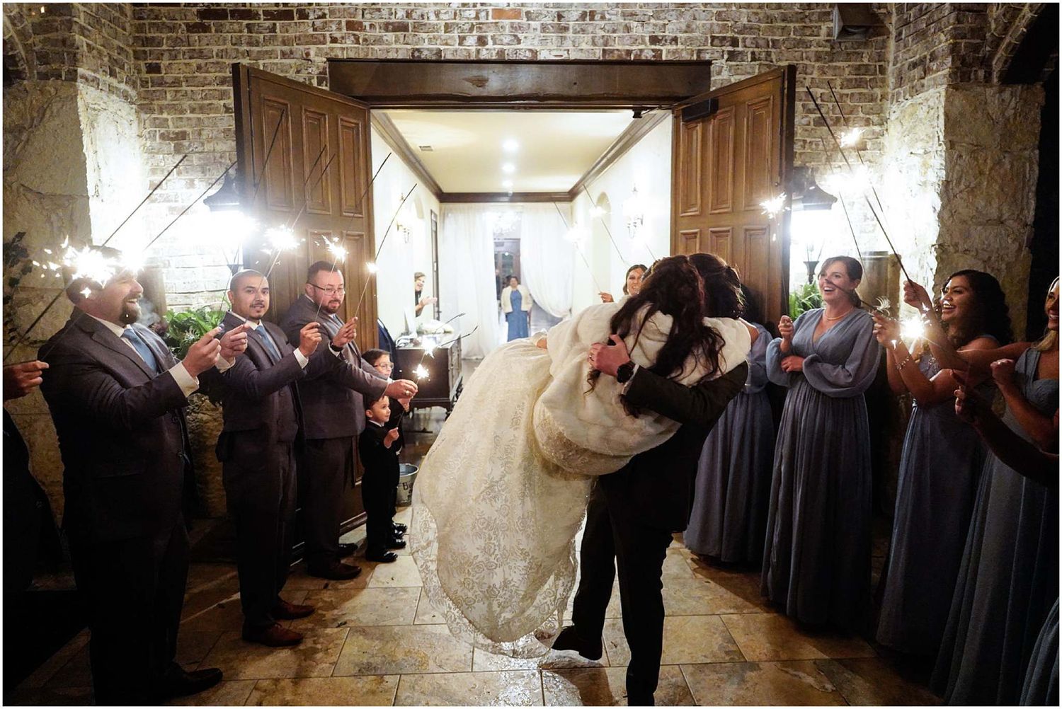 Groom lifts bride in romantic dip during sparkler exit at rustic stone wedding venue.