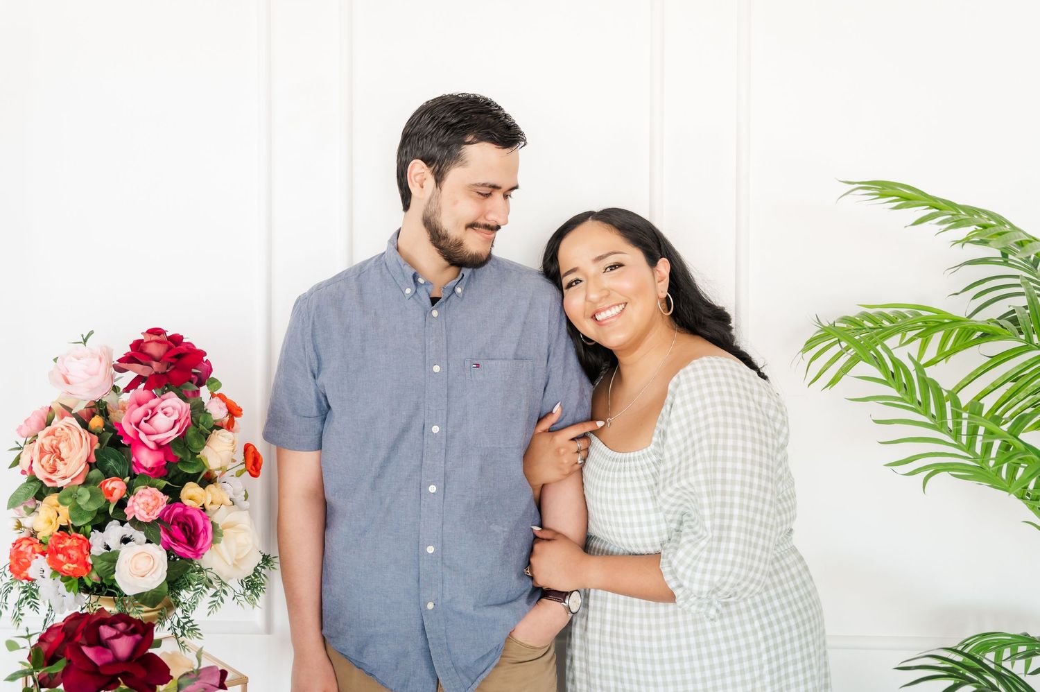 A romantic portrait of a couple posing together with pink floral arrangements and greenery.