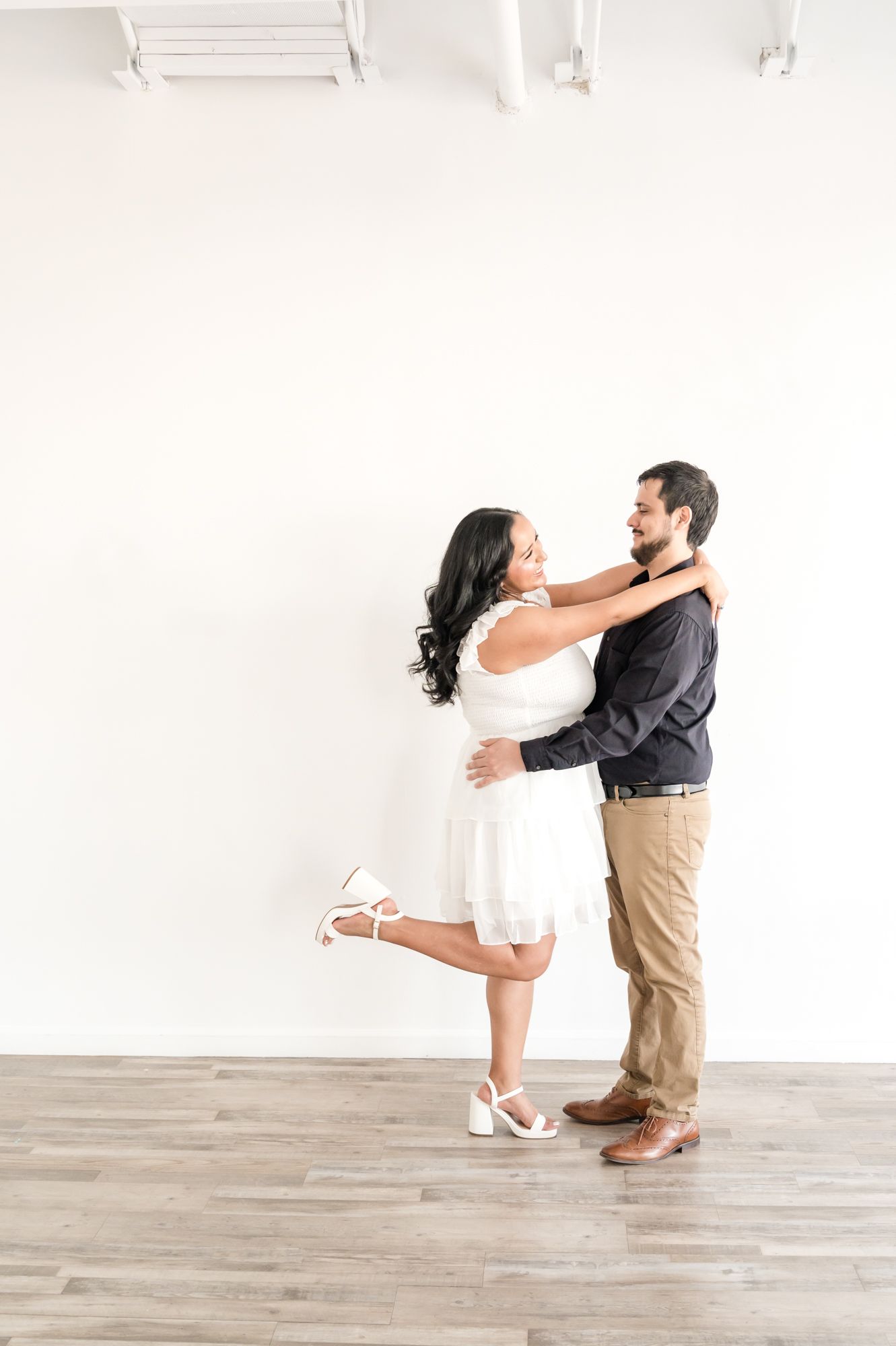 A playful couple performs a dip dance move on a light wooden floor in a white studio.