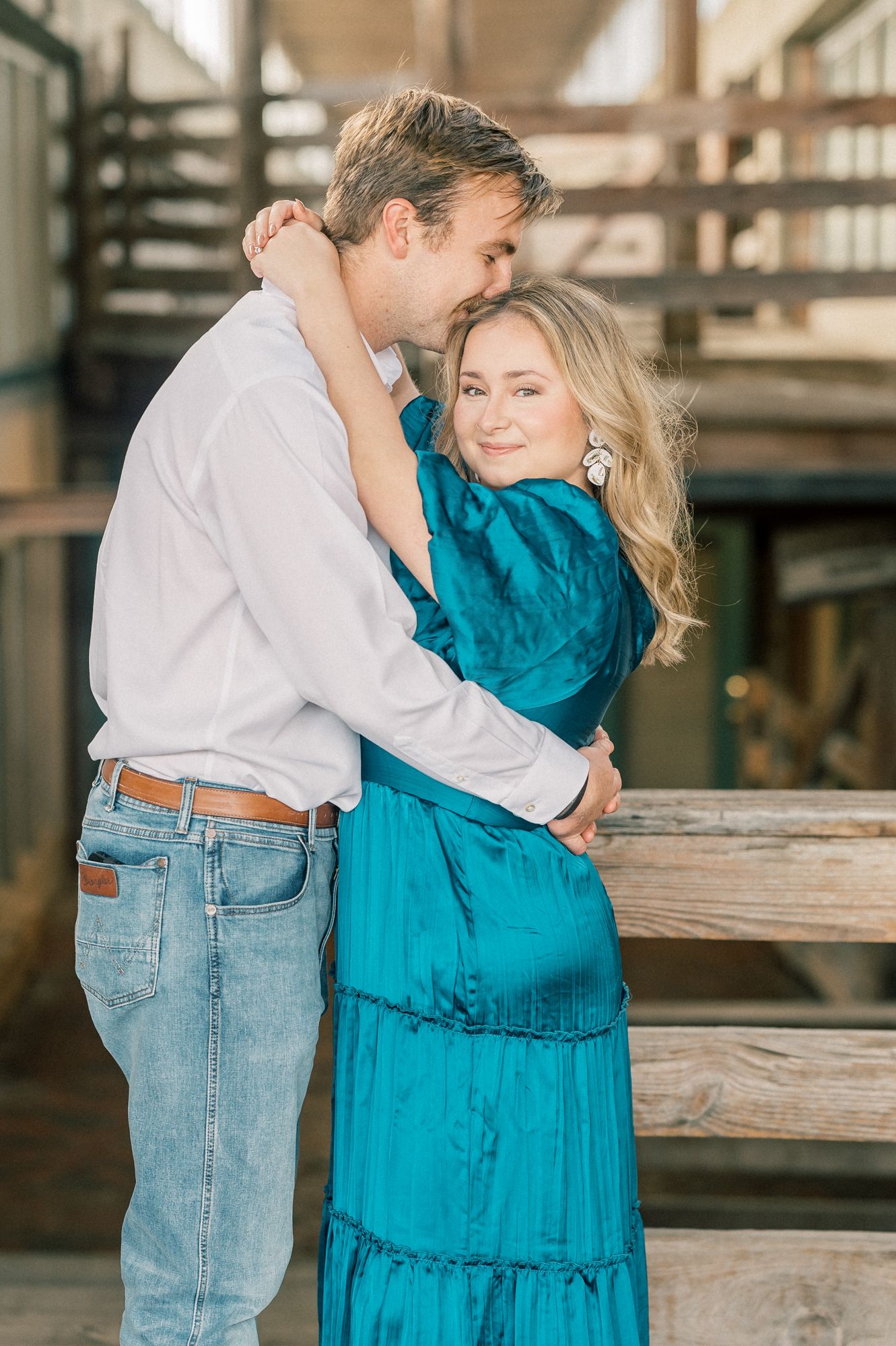 A romantic moment captured between a couple in casual attire standing by wooden railings.