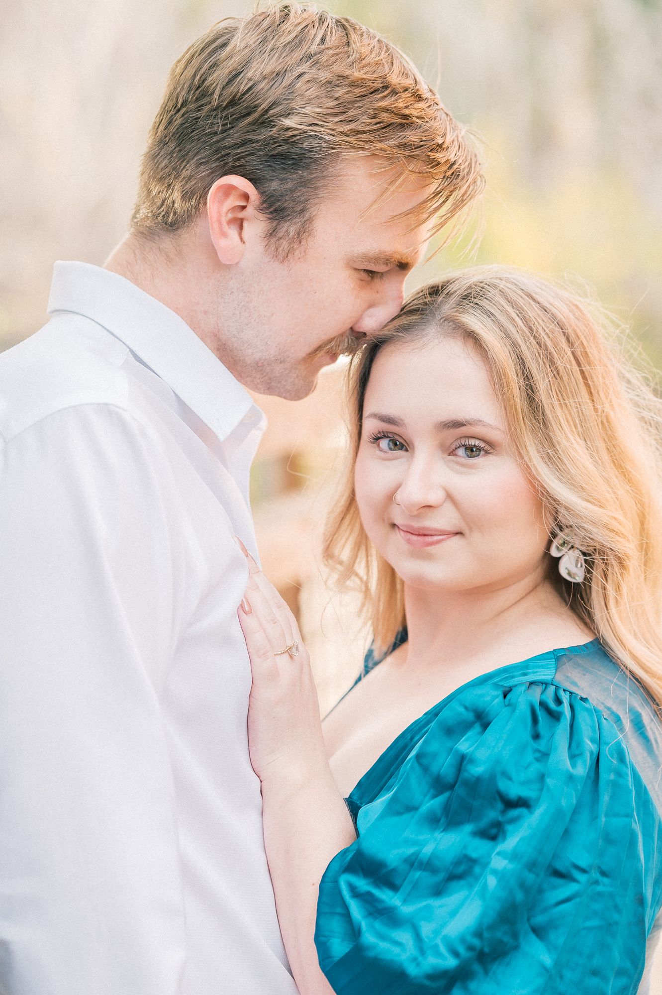 A tender moment between a couple during their engagement photoshoot wearing white and teal outfits.