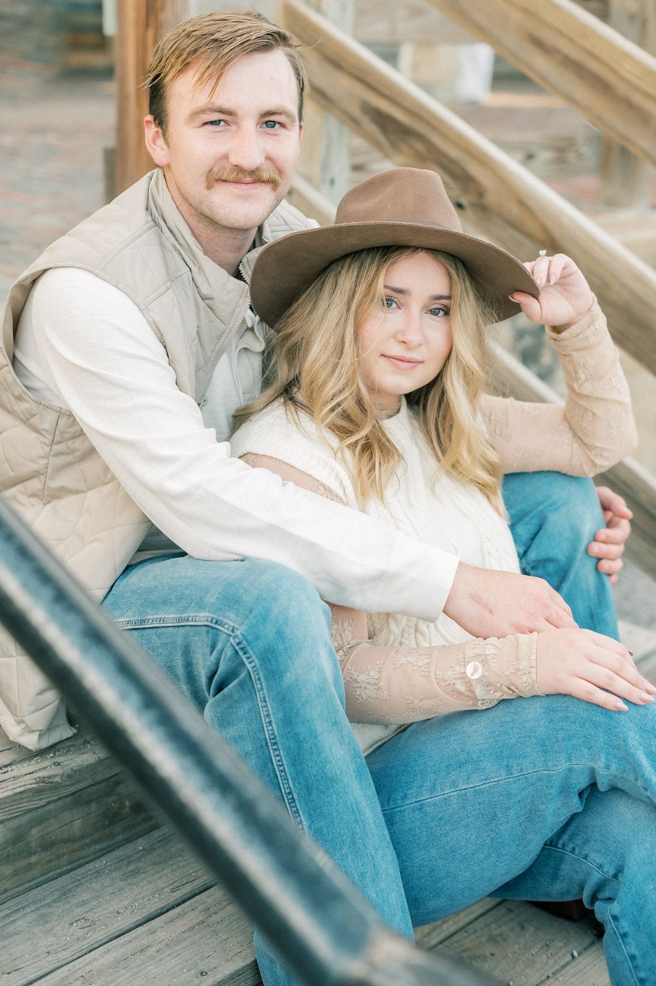 A couple in denim and western wear posing together on rustic wooden steps.