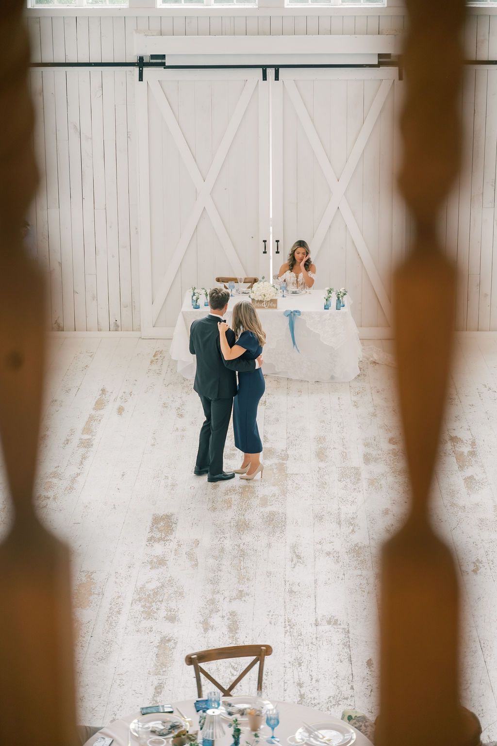 Aerial view of couple dancing in a white barn wedding venue with rustic wooden floors and barn doors.