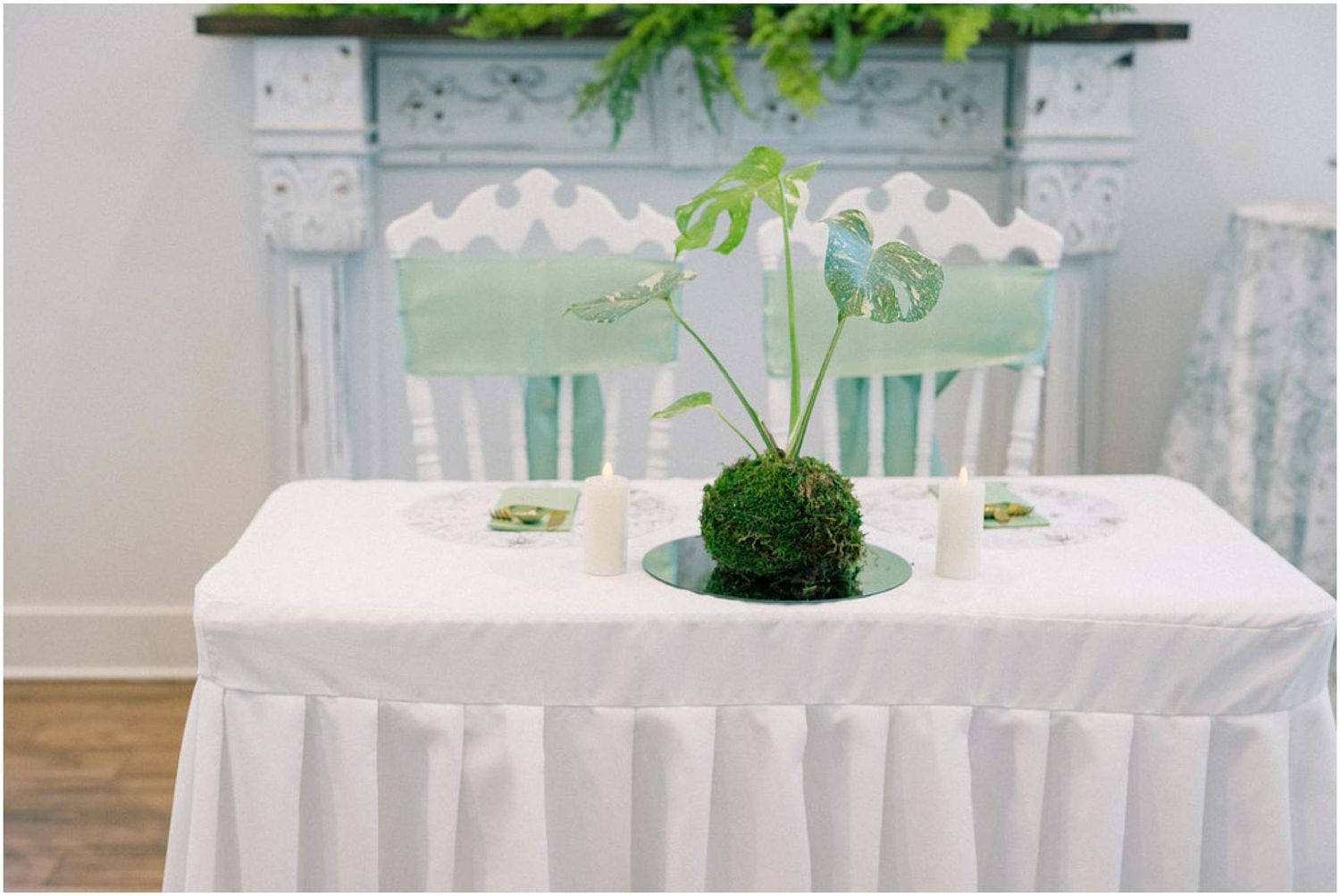 Elegant white tablecloth covered table with a green moss centerpiece and delicate floral accents.