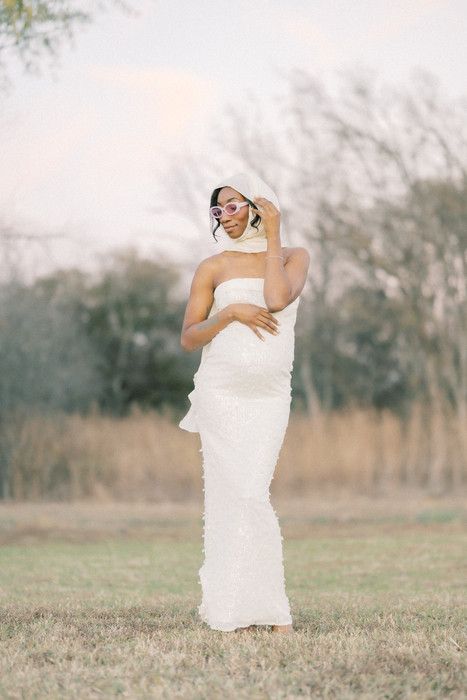 An artistic portrait of someone wrapped in flowing white fabric standing in a sunlit meadow.