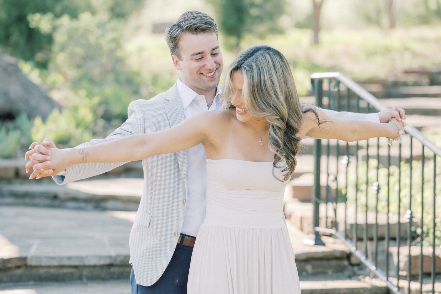A couple shares romantic moments during their wedding photoshoot in a sunny outdoor garden setting.