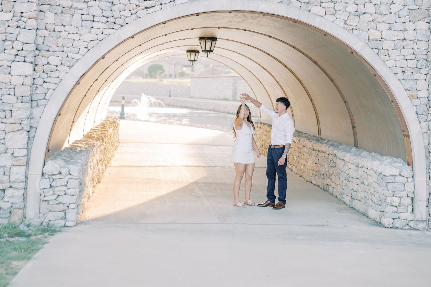 Couple holding hands under a stone arch tunnel during an outdoor engagement photo session.