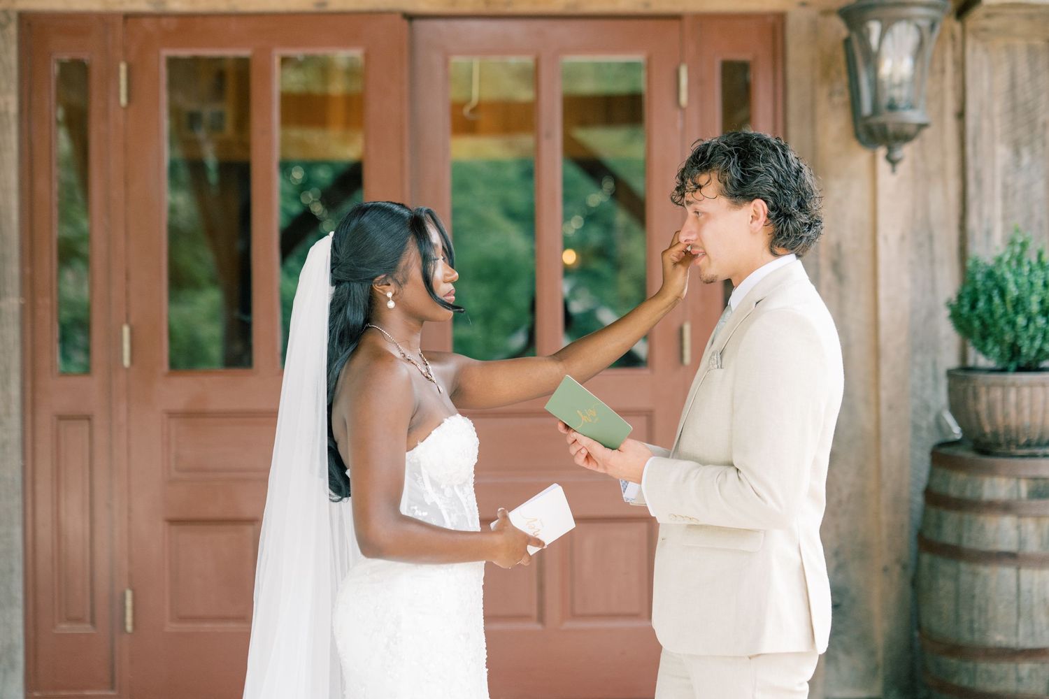 Bride and groom share emotional vow exchange outside wooden doors at their wedding ceremony.