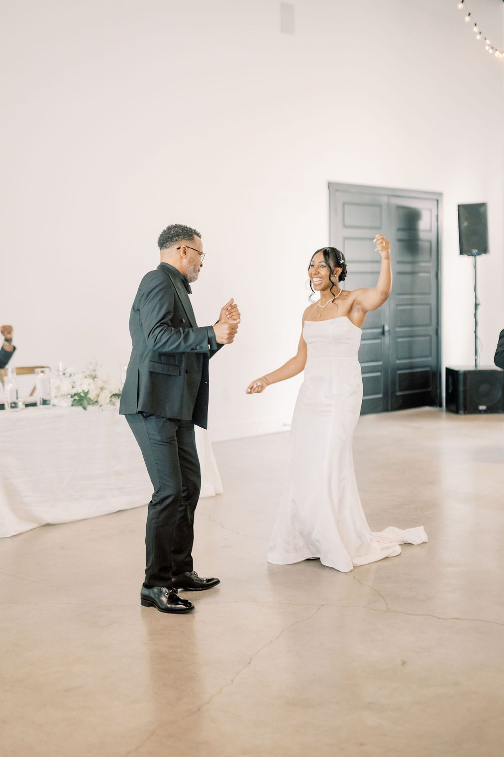 Bride and groom share a joyful first dance in an elegant white reception hall during their wedding celebration.