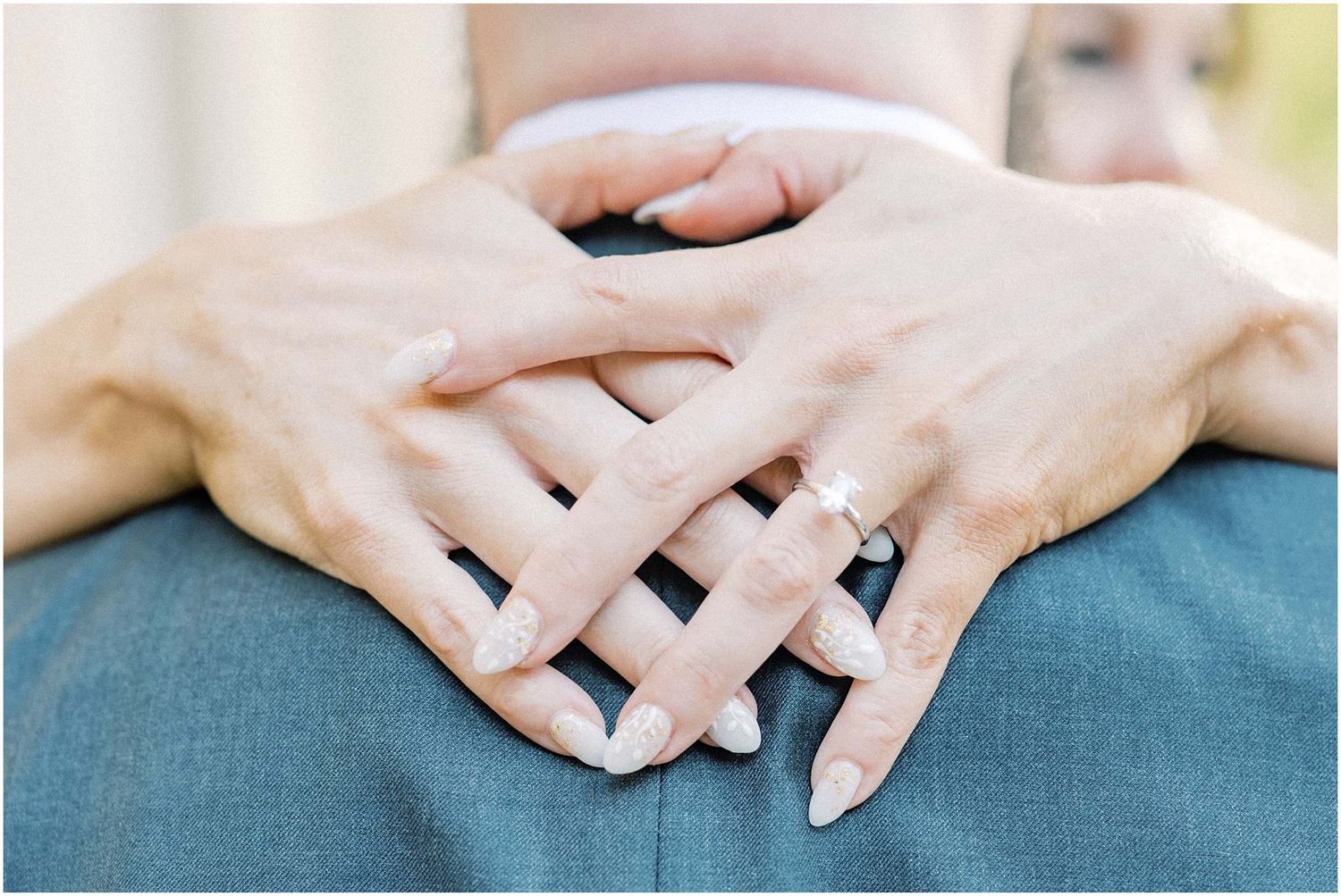 Close-up of hands with interlaced fingers resting on blue fabric.