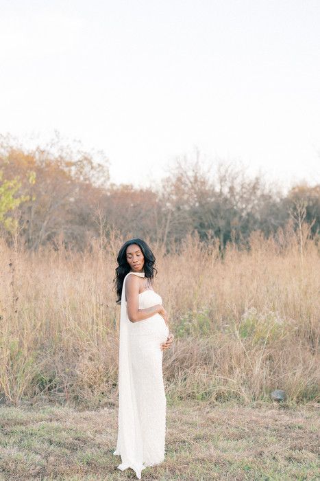 A figure in a flowing white dress poses gracefully in a golden autumn field during a photoshoot.